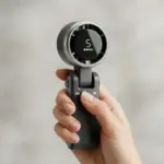 Hand gripping a gray handheld portable fan with a circular display showing the number 5 and small battery indicators.