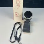Ring light on a swiveling mount with a rectangular battery pack, accompanied by a product box showing diagrams; black lanyard cables lie nearby on a light surface.