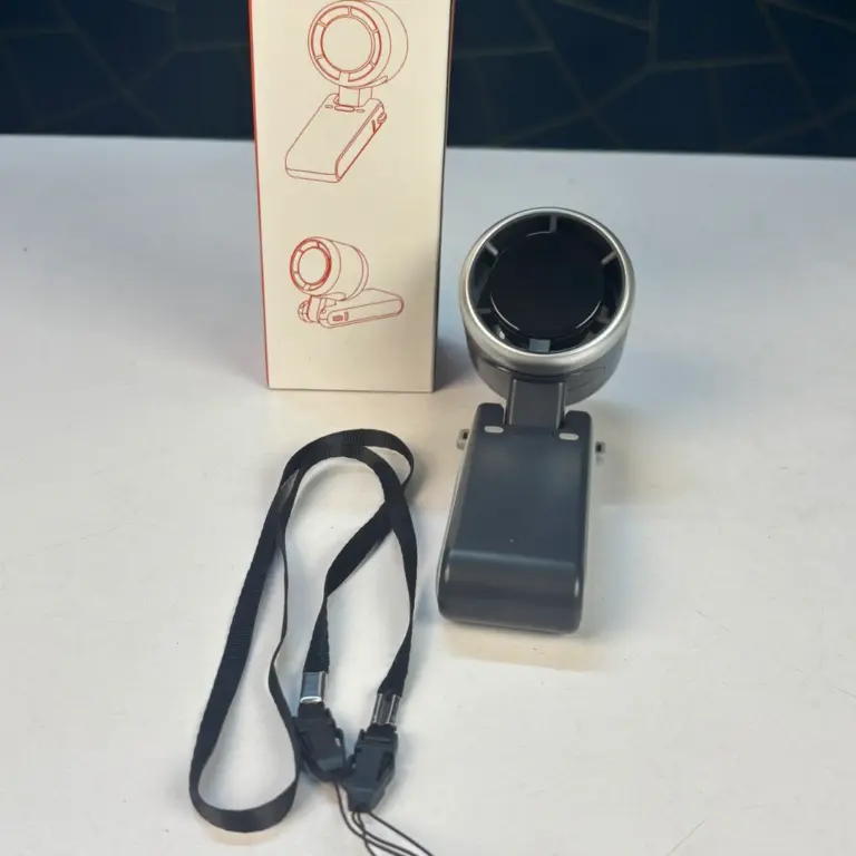 Ring light on a swiveling mount with a rectangular battery pack, accompanied by a product box showing diagrams; black lanyard cables lie nearby on a light surface.